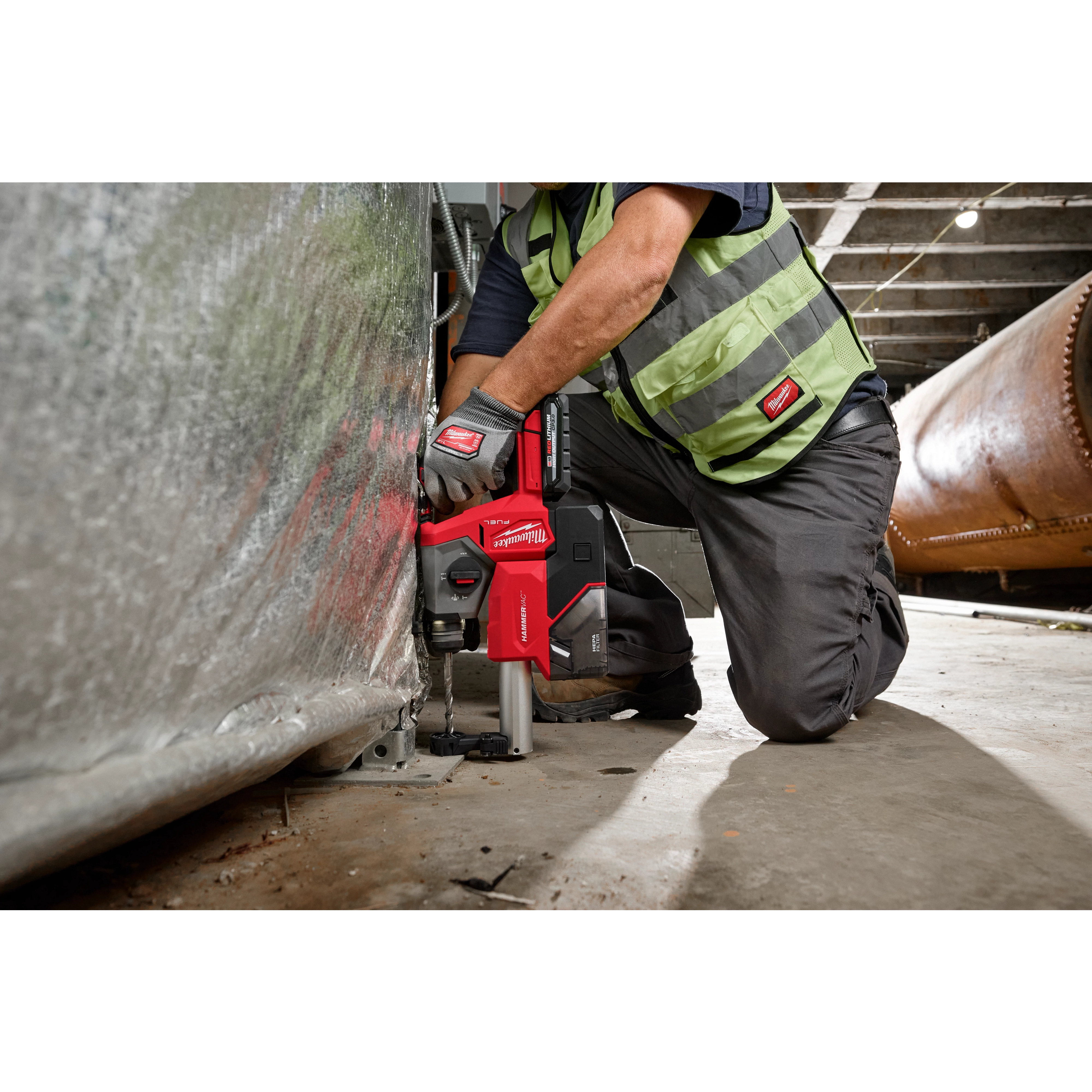 A worker in safety gear uses an M18 FUEL™ 5/8" SDS Plus Rotary Hammer with Dust Extractor Kit to drill into a metal surface inside an industrial setting.