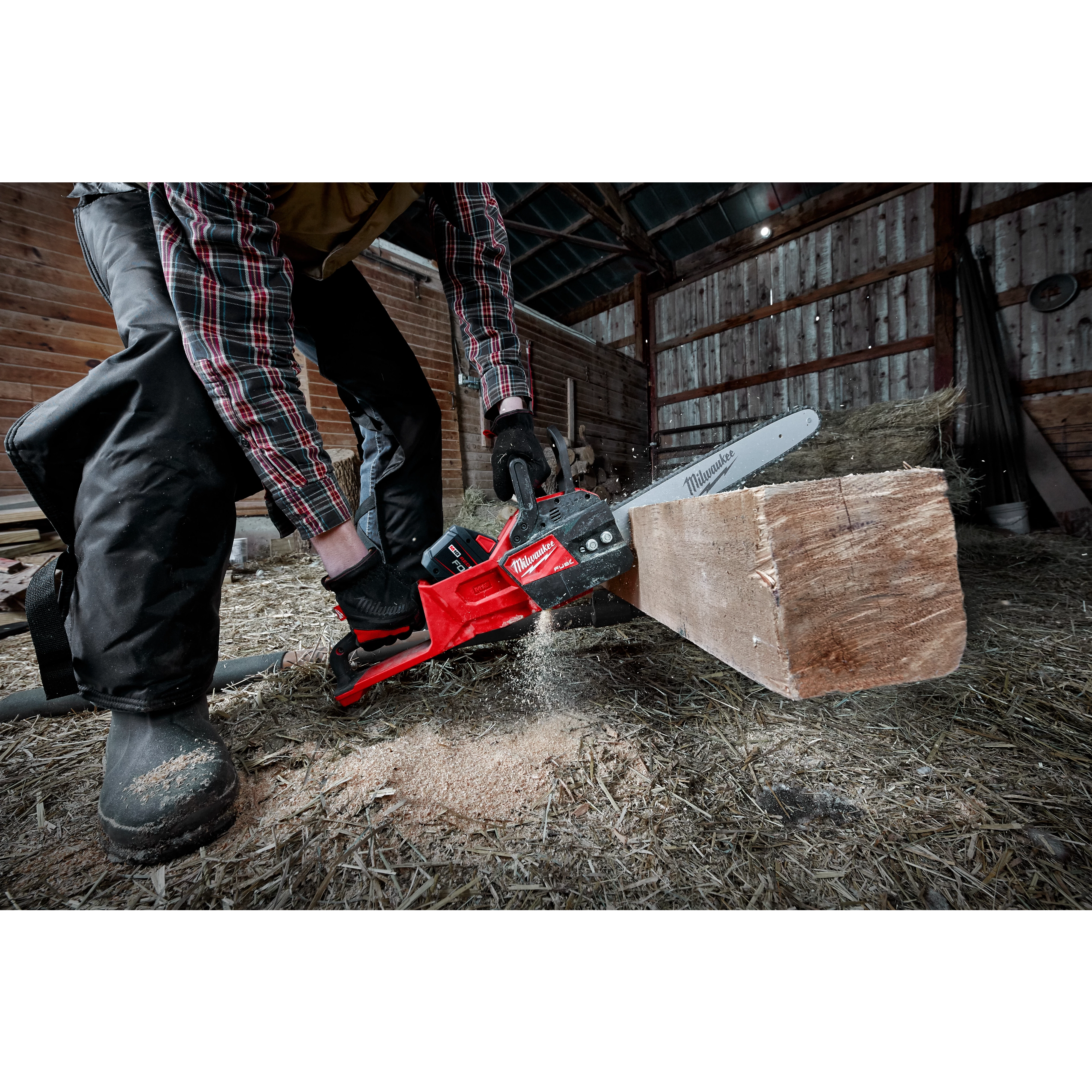 Person using a red chainsaw to cut through a wooden log inside a rustic barn.