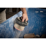 A person holds a dust-covered filter from the M18 FUEL™ 3-in-1 Backpack Vacuum over a blue container, likely for cleaning or replacement.