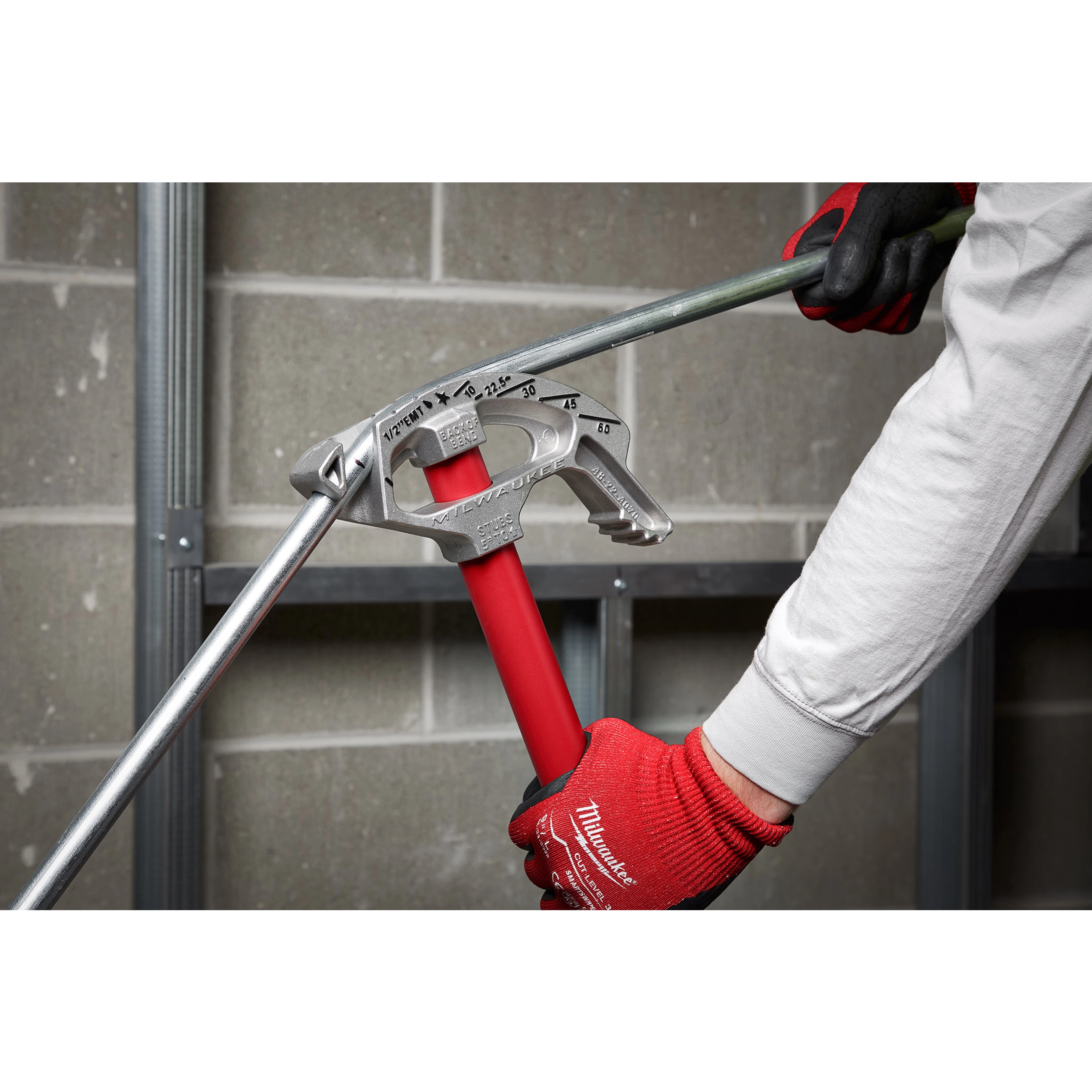 Person using 1/2" EMT Aluminum Conduit Bender with red handle to bend a metal conduit against a gray brick wall.