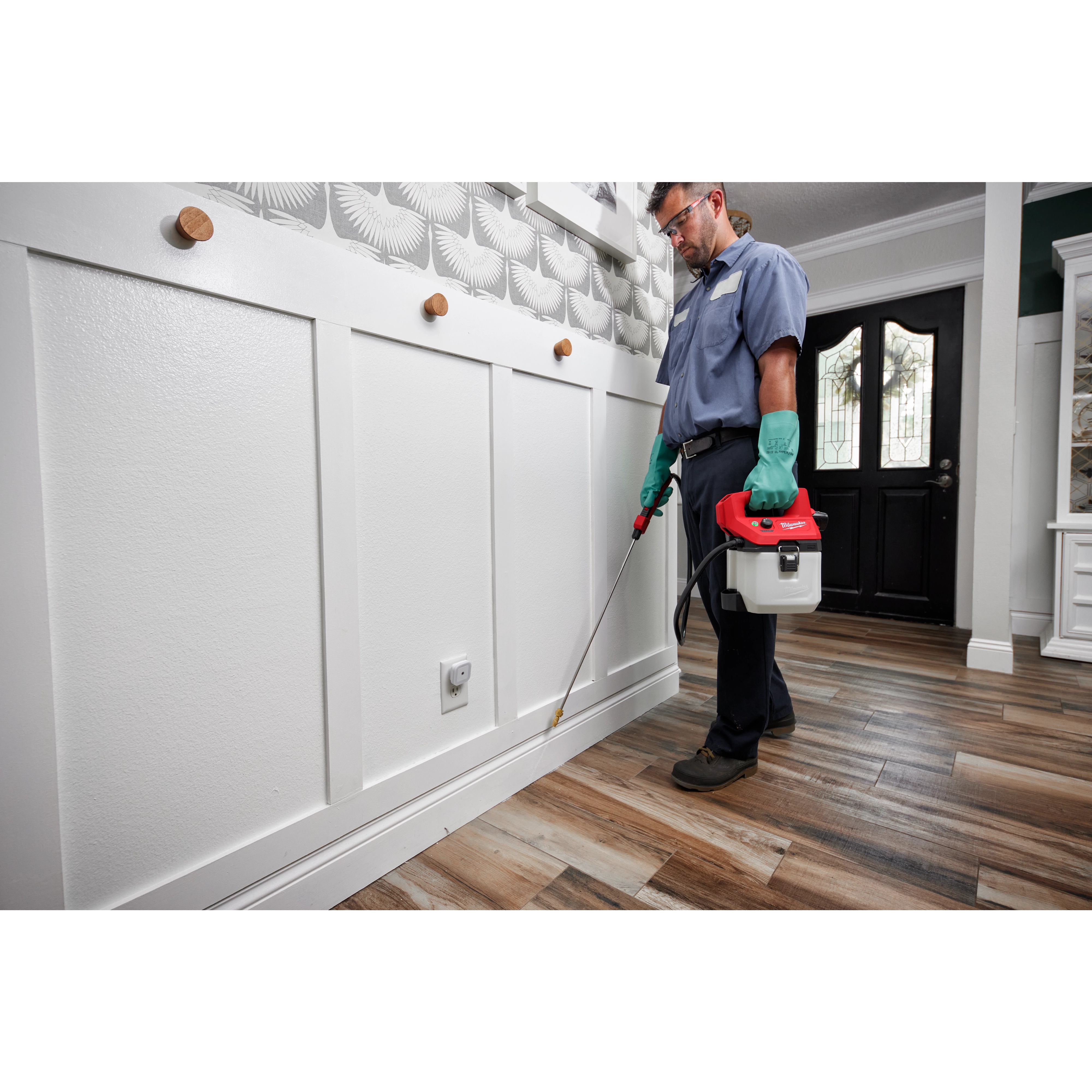 Man using the M12 Handheld Sprayer to spray along wall trim indoors for pest treatment