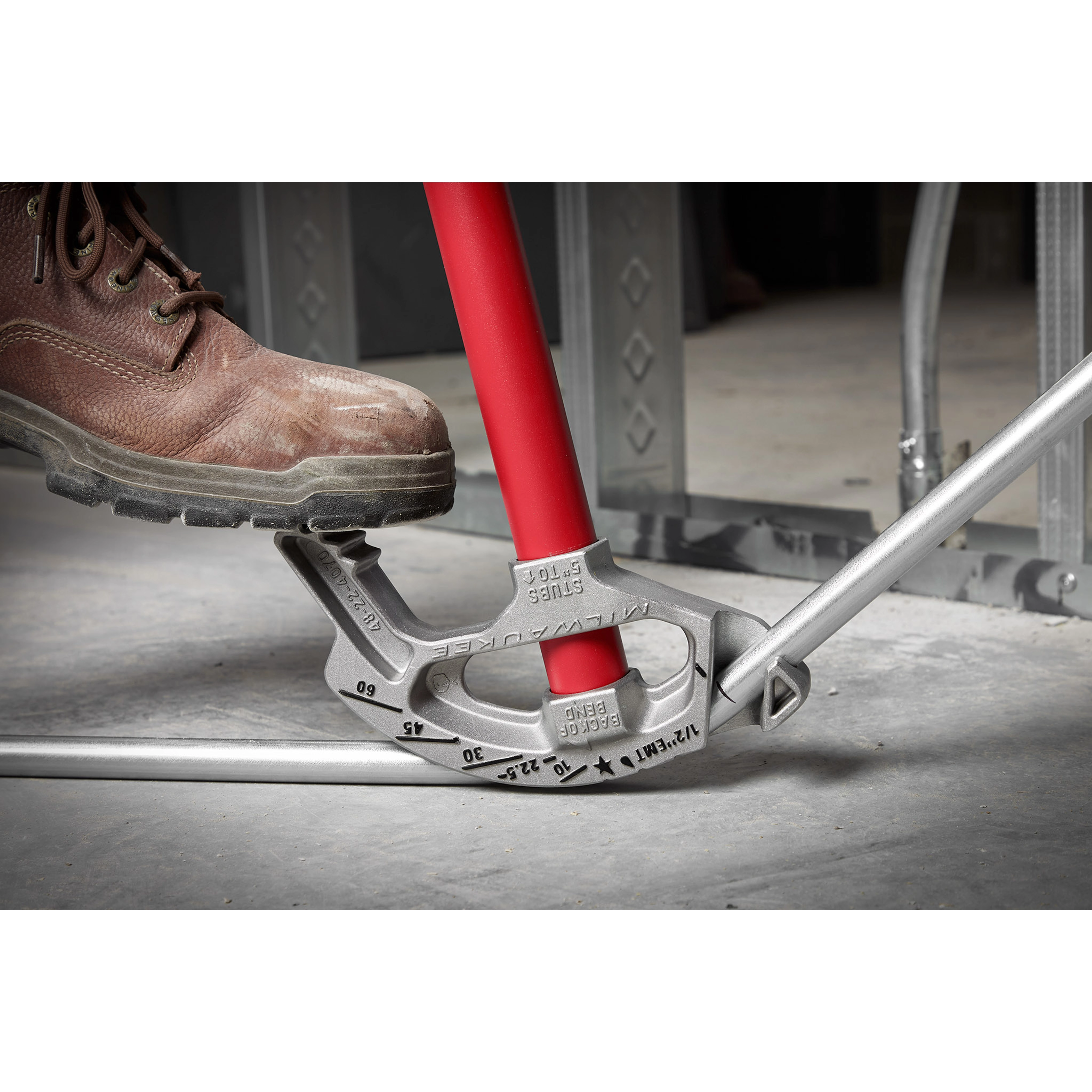 1/2" EMT Aluminum Conduit Bender with red handle being used by a person wearing a work boot to bend a metal conduit pipe.