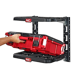 Hand placing a red tool storage box onto the PACKOUT Racking Kit's black shelving, which is mounted on a wall.