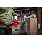 Person in a workshop using a Milwaukee chainsaw to cut a large wooden beam, with sawdust flying.