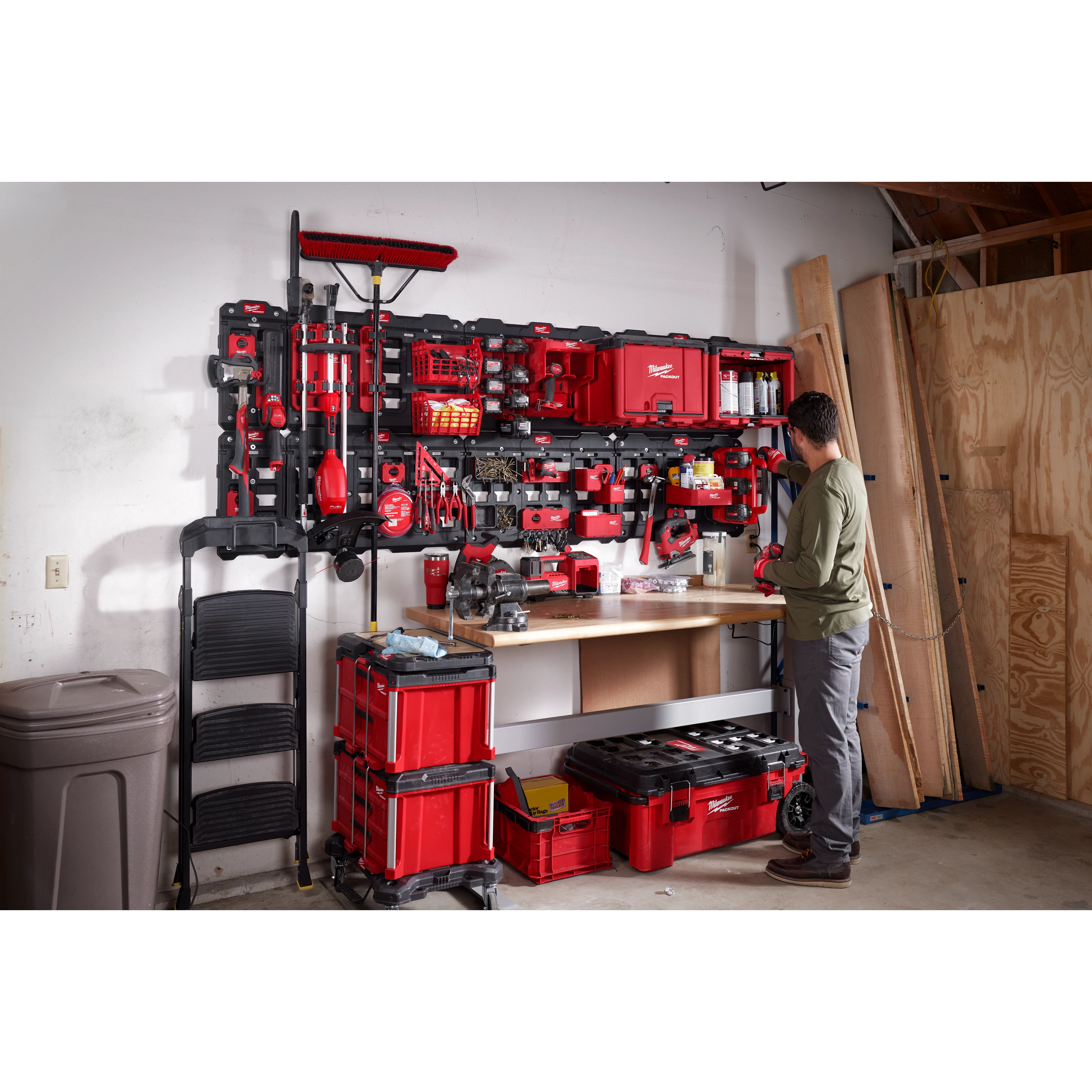 Man organizing tools on a wall-mounted March 2023 Packout Shop Storage system in a well-equipped garage workspace.