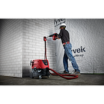 A worker uses the Vacuum, M18 FUEL™ 1-9/16" SDS Max Rotary Hammer, SDS Max Dust Extraction Attachment, and M18 FUEL 1-9/16" SDS Max Hammer Drill to chisel a white brick wall. The setup includes a red and black vacuum connected to the hammer drill for dust extraction.